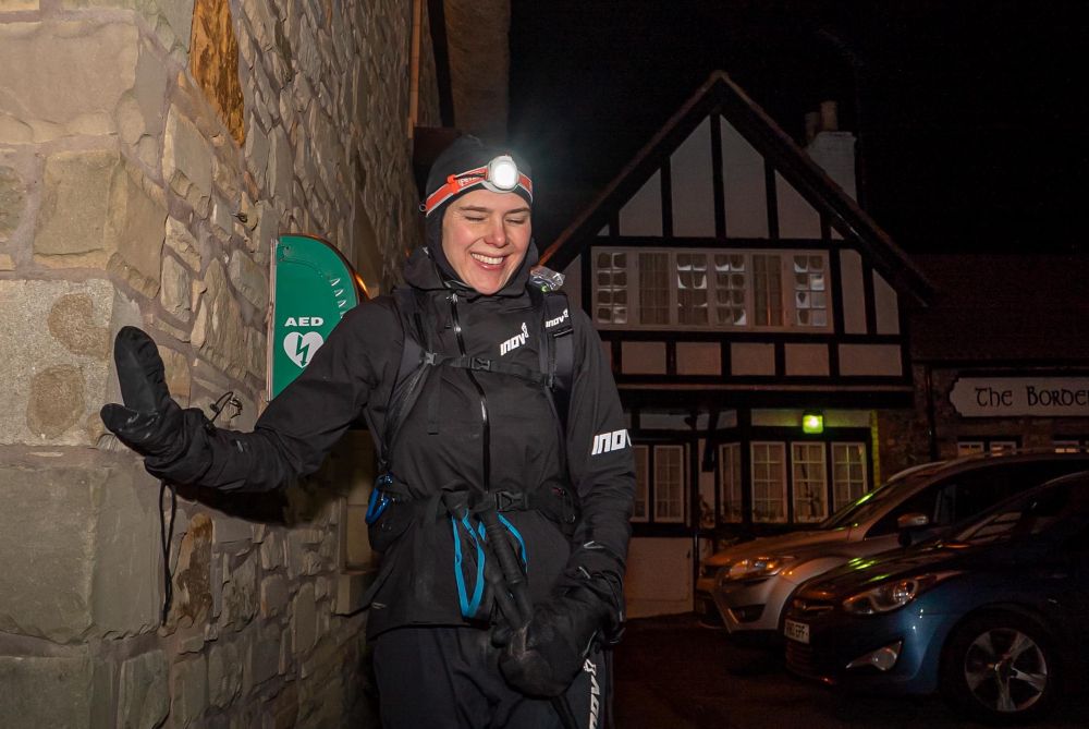 Jasmin Paris smiling and looking extremely happy at the wall of the Border Hotel in Kirk Yetholm. She has just won the #SpineRace and taken 12hrs off the CR.