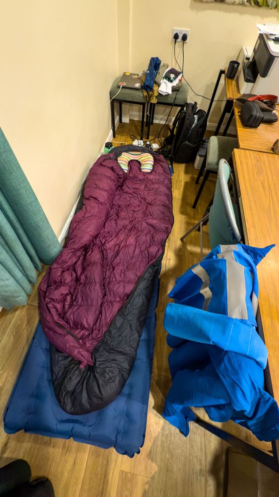 A blow up mattress, sleeping bag and other kit strewn on the floor, behind the registration desks at Edale Village Hall #SpineRace 