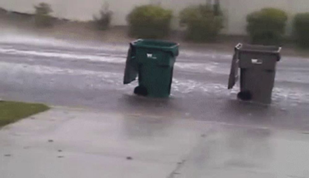 two garbage cans are sitting in the rain on a sidewalk