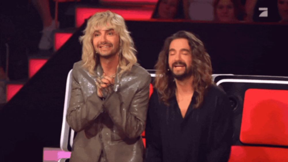 a man with blonde hair and a beard is sitting next to another man with long hair