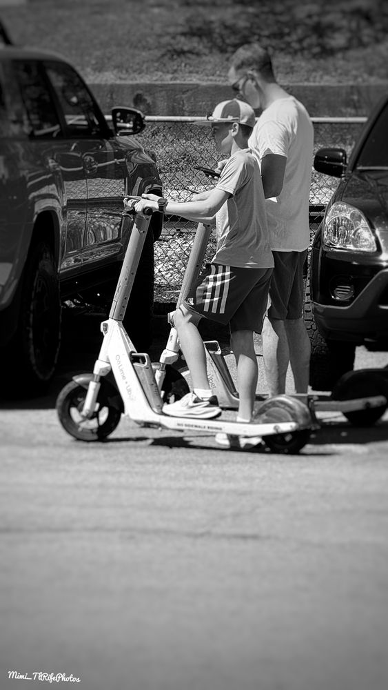 A black and white photo of a father and a son on electric scooters.