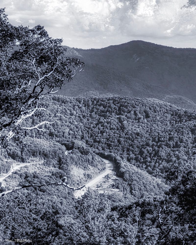 A black-and-white photo of mountains, looking down at a road. June 2024