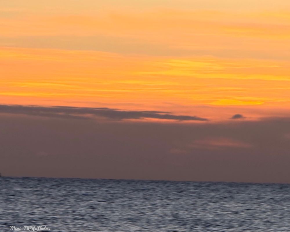 A sunset of yellow, orange, peach, and a dark gray color. The ocean is dark in color. 