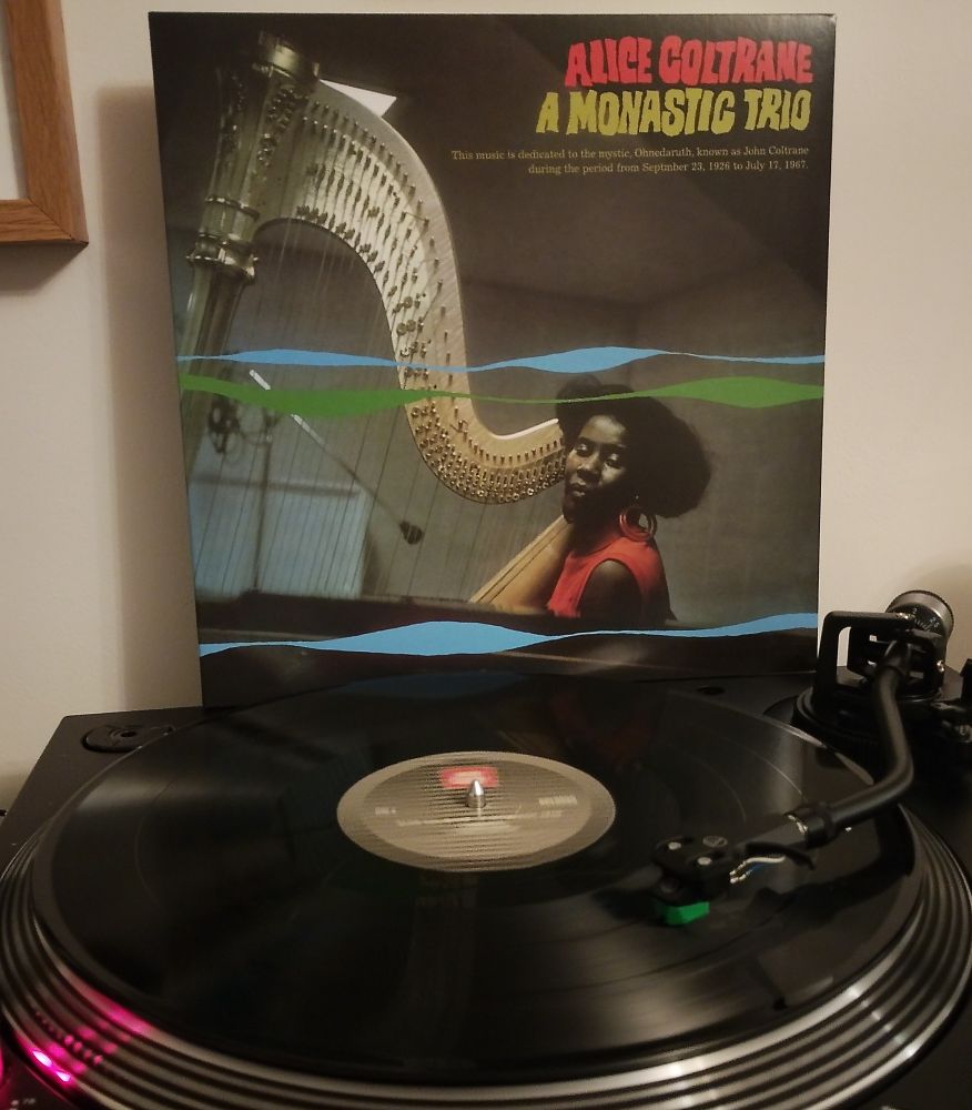 Black vinyl LP playing with album sleeve behind.
A colour photo of Alice sat at her harp. Under the title of the album it reads: This music is dedicated to the mystic, Ohnedaruth, known as John Coltrane during the period from September 23, 1926 to July 17, 1967.