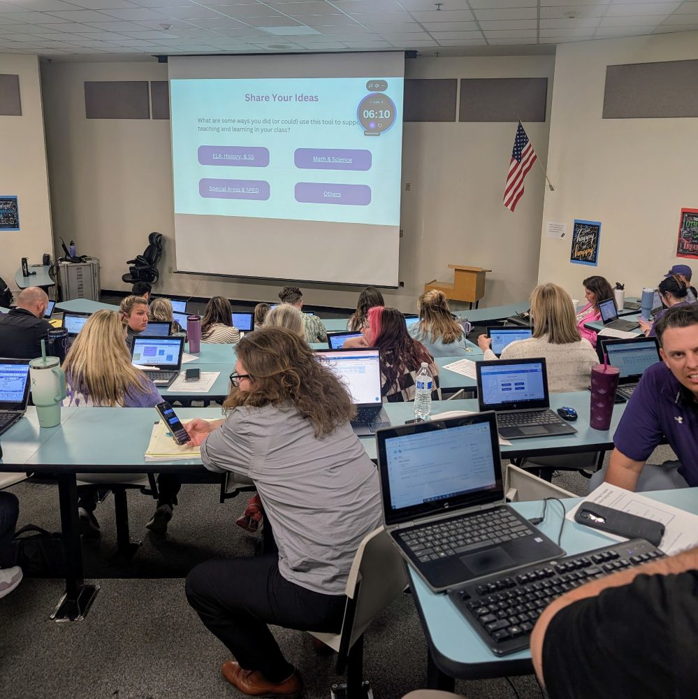 A room full of teachers on laptops facing a projector screen.