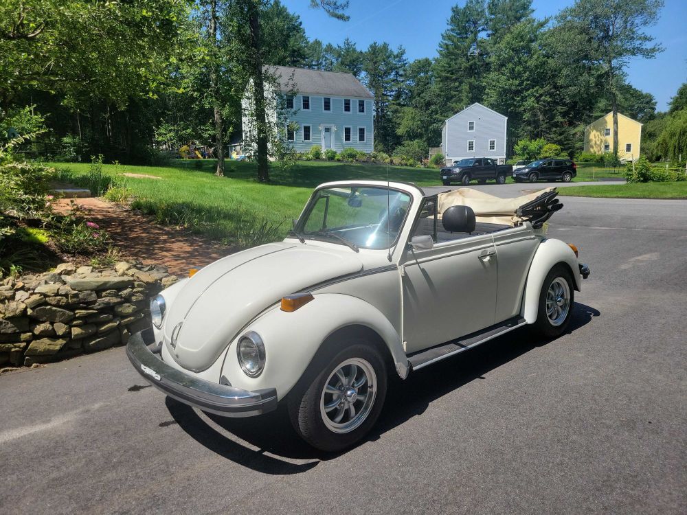 A white 1979 vw superbeetle convertible, parked, with the top down, in the driveway of a residential neighborhood. 