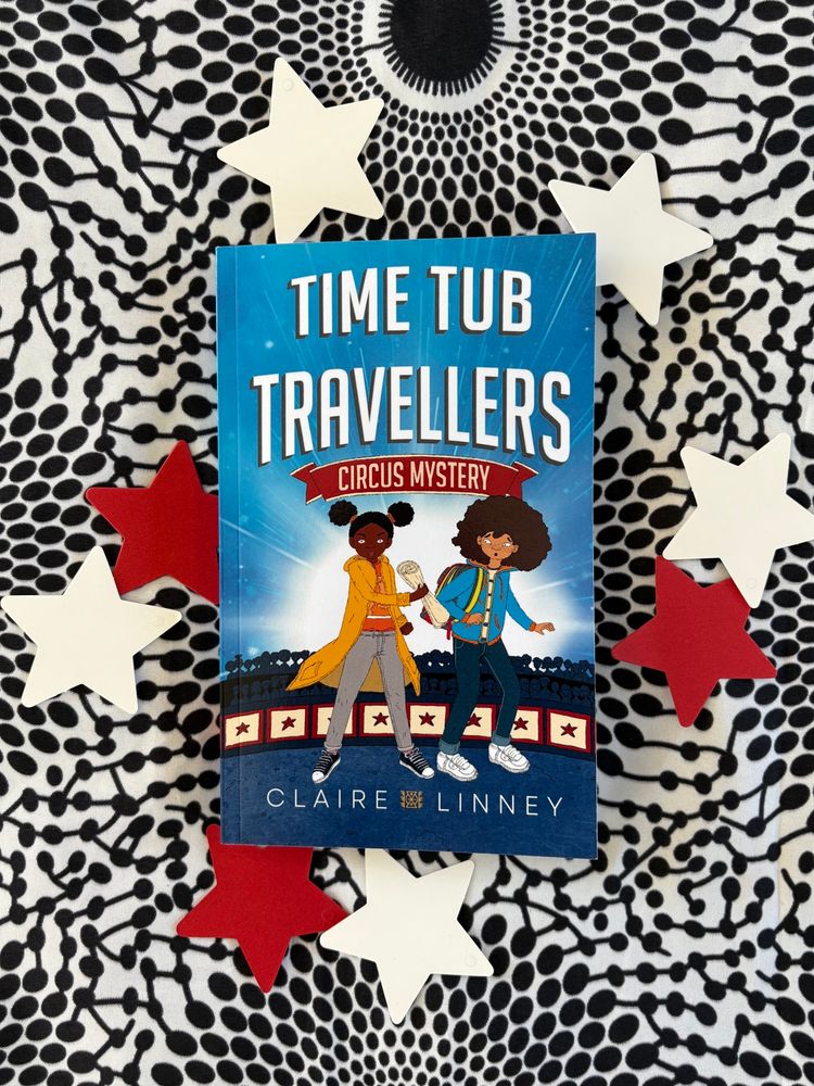 The book Time Tub Travellers: Circus Mystery by Claire Linney is nestled on red and white stars on a patterned African print fabric background 