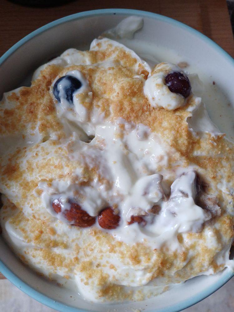 A round breakfast bowl with yoghurt and orange flax seed, seen from above, so that it looks like a face - with grapes for eyes and almonds forming a sort of droopy smile