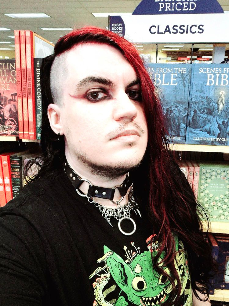 Goth guy in a book store with half shaved head and a collar.