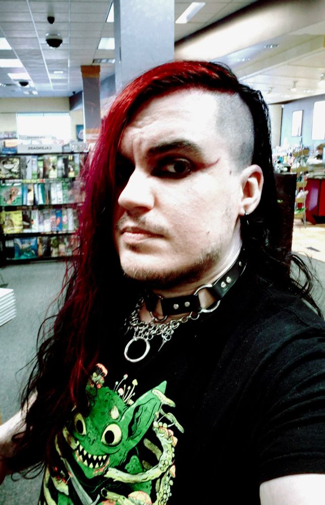 Goth guy in a book store with half shaved head and a collar.