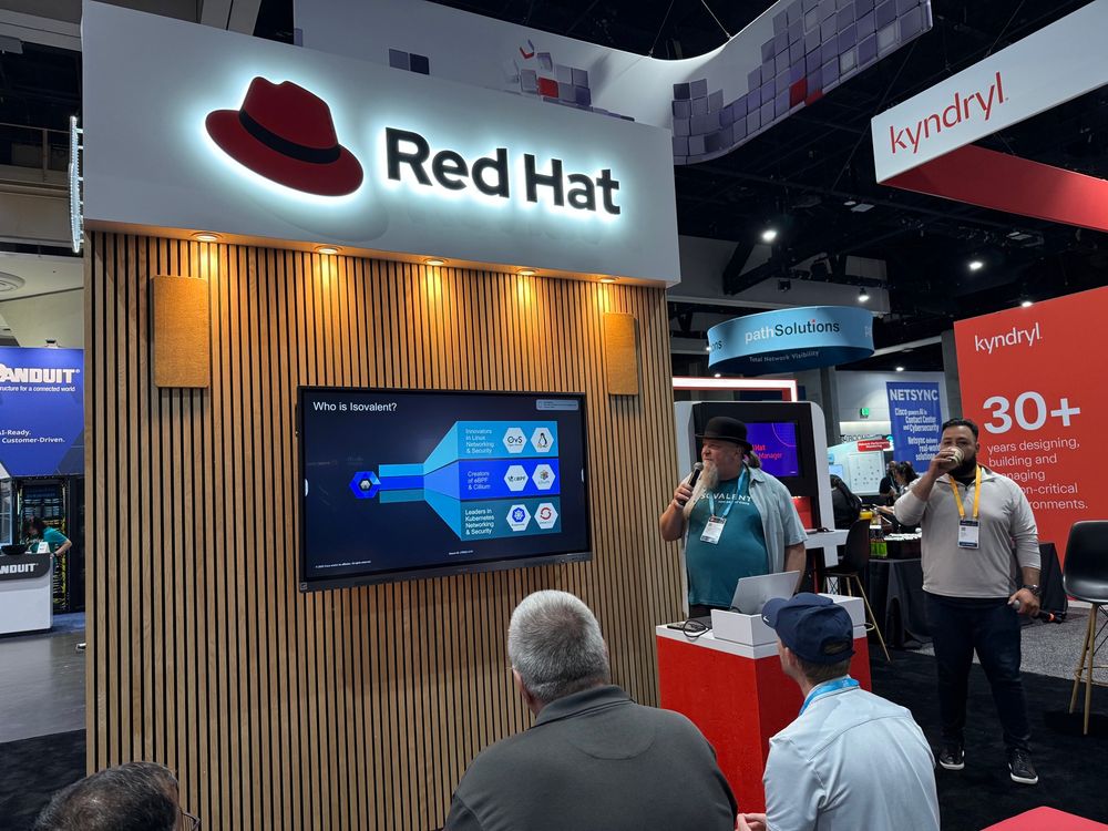 Red Hat conference booth, Duffie presenting in his trademark bowler hat, slide showing Isovalent