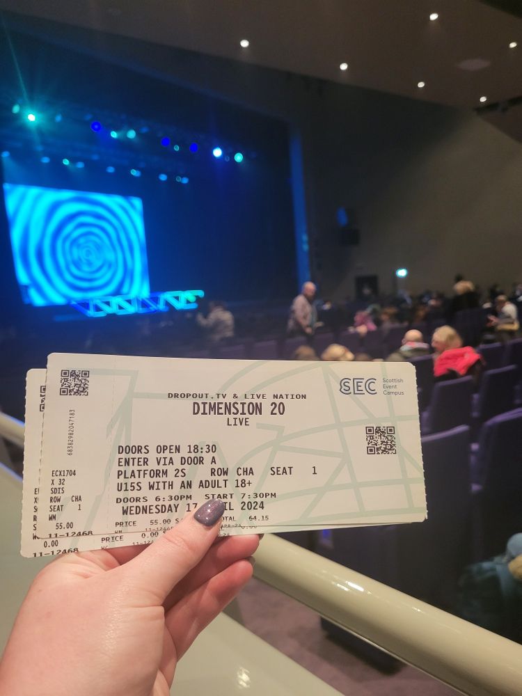 A photo of Dimension 20 Live tickets with a stage in the background featuring a blue spiral screen