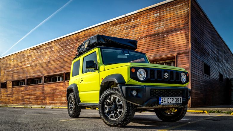 bright green two door suv with a roof tent and big tires. in front of an old warehouse building. 