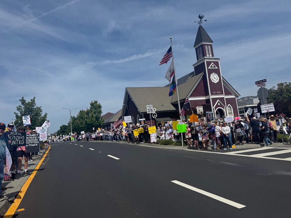 old school red and white city hall building, the sides of the road in front covered in hundreds of anti Trump protestors with signs 