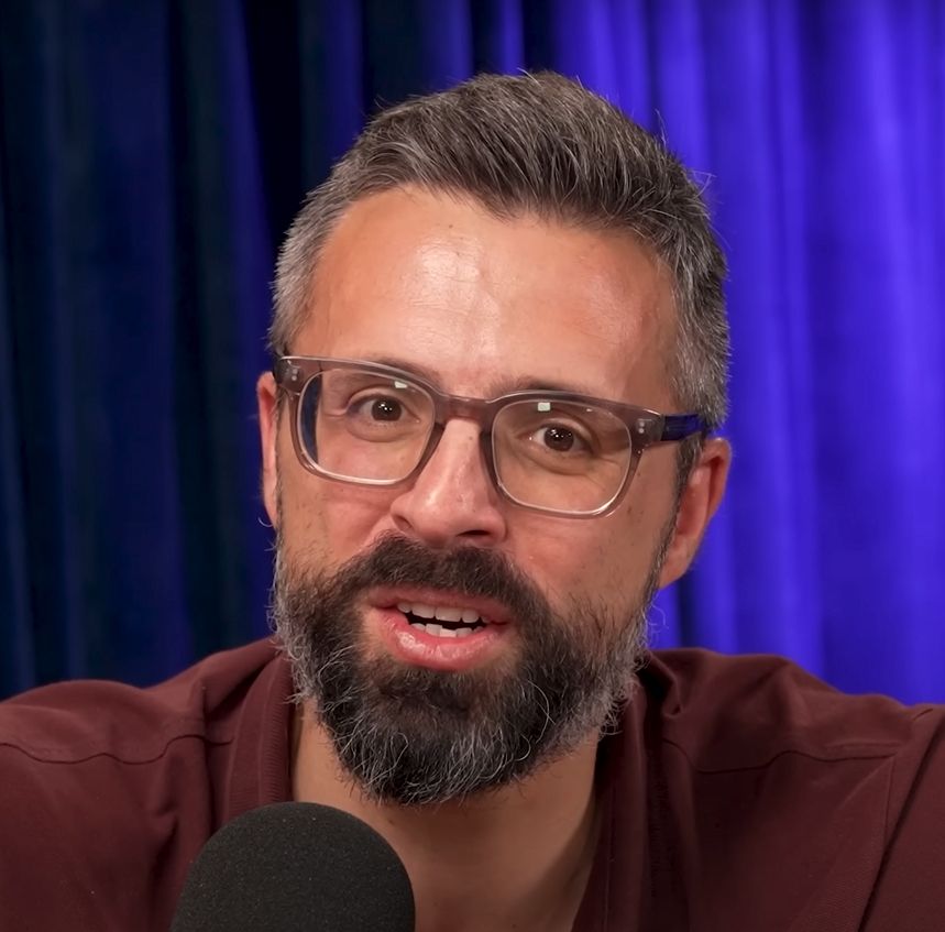 white dude with glasses, salt and pepper hair and scraggly beard, talking into a microphone probably saying something scolding about leftists