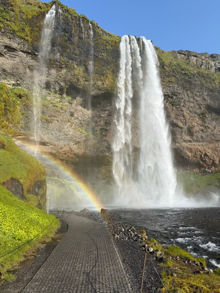 Photo of a waterfall in Iceland, with a rainbow in the spray at the bottom of the falls. 