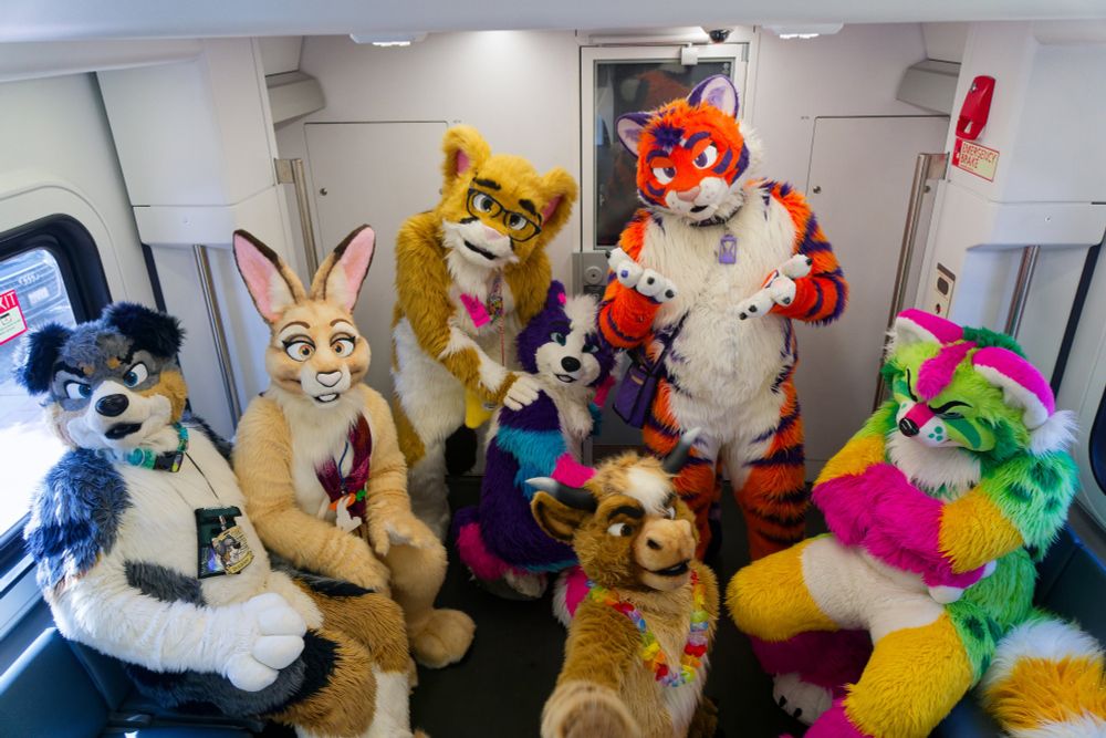 A whole bunch of cute fursuiters posing inside a Caltrain car. 