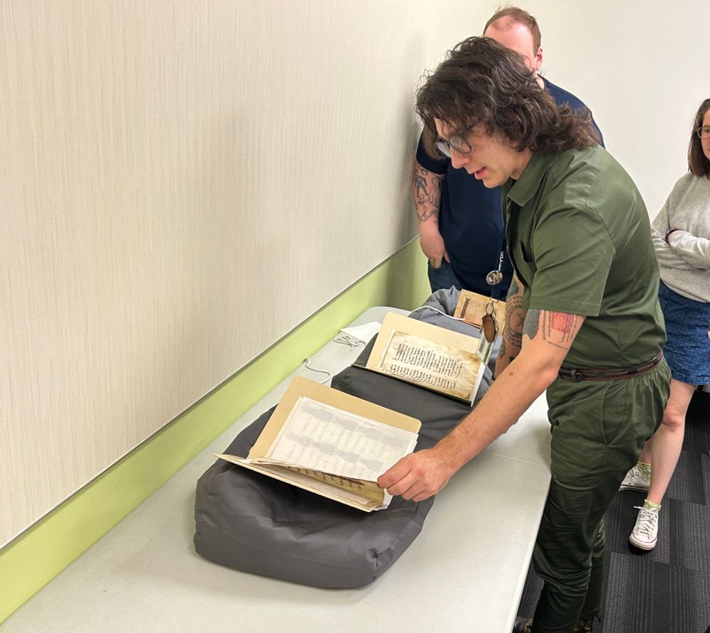 Devin standing in front of a table laid with three open manuscripts.