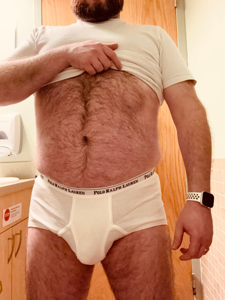 A thighs-to-chin photo of me in a pair of Polo Ralph Lauren white briefs, lifting my white tee to show my hairy belly. My big bulge sits between my hairy thighs.