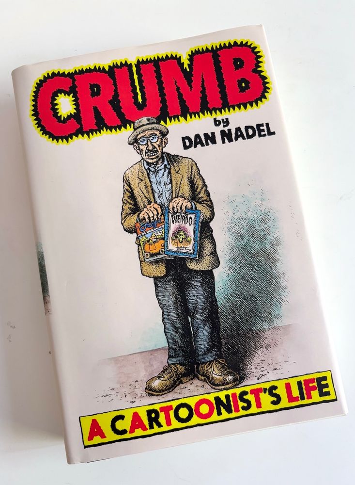A self-portrait by Robert Crumb adorns the front cover of the book. The artist is seen standing against a white background holding two of his publications; a copy of Zap Comix and a copy of Weirdo. The titles--drawn by hand as well-- are in bright red, yellow and black.