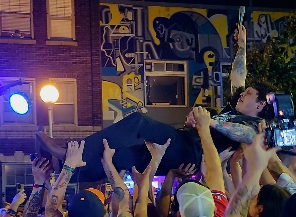 John Spinney from Monsterwatch crowd surfin' during their set, with the microphone held high in his right hand.