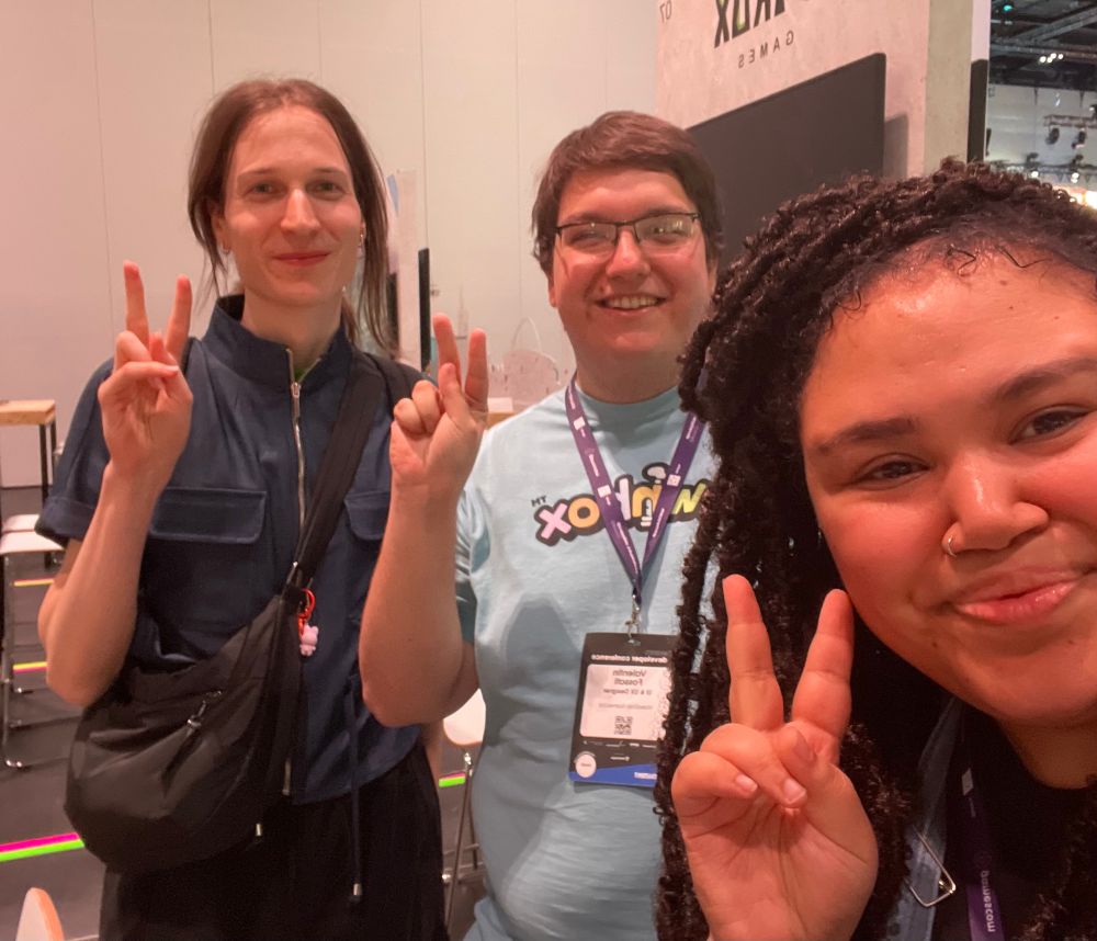 It’s me and the users/developers mentioned in the post. I have dark brown locs, tan skin, wear a black shirt and a blue jumpsuit over it, I’m smiling showing the peace sign. Behind me are the devs, one with long hair tied back and a dark blue zipper shirt and black pants, hair blonde and eyes grey-ish blue and also smiling and showing the peace sign. Next to him the dev has short brown blond-ish hair and wears glasses, wears a baby blue townbox game shirt and he is smiling and showing the peace sign as well.