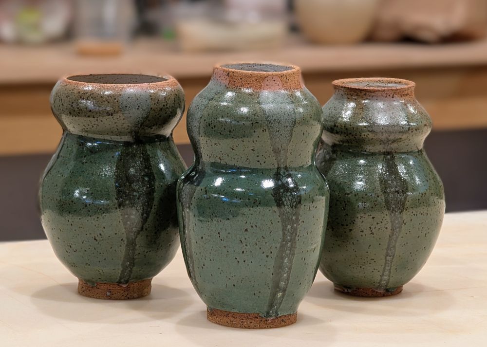 Three small green bulbous vases. Hand thrown. They are a shiny green color.