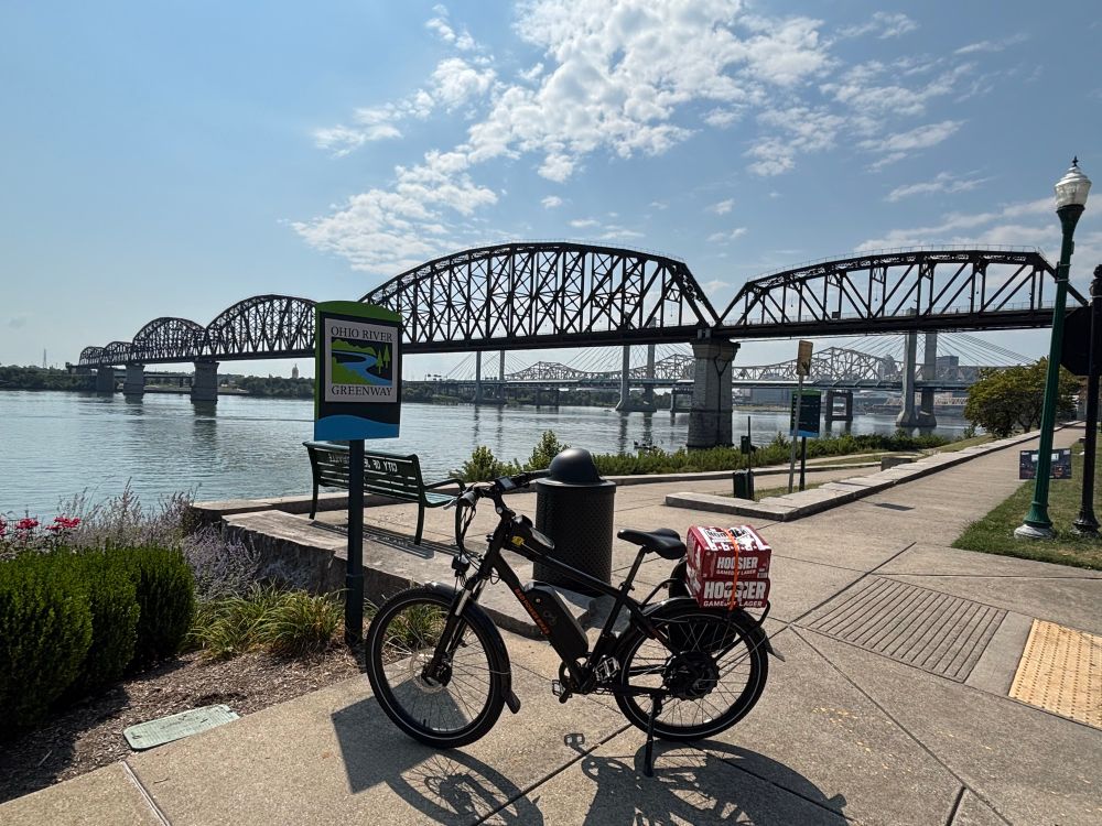 A bike in front of a bridge with beer strapped to it 