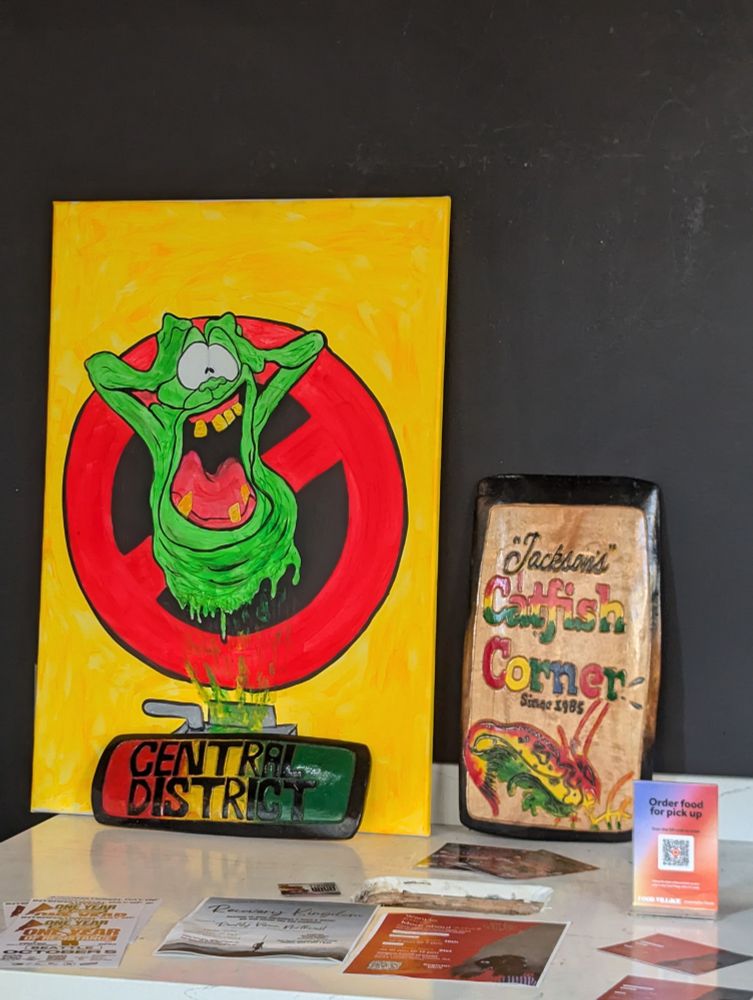 A painting of cartoon Slimer from The Real Ghostbusters being trapped by a red, yellow, and green rectangular object with the words "CENTRAL DISTRICT", the name of an area of Seattle historically recognized as the local center of Seattle's Black community in the 20th century, thanks in significant part to exclusion in other parts of the city. The art is displayed inside the Seattle restaurant Jackson's Catfish Corner, which has the best catfish in Seattle according to the writer of this text, who spent their first three decades of life in Tennessee.