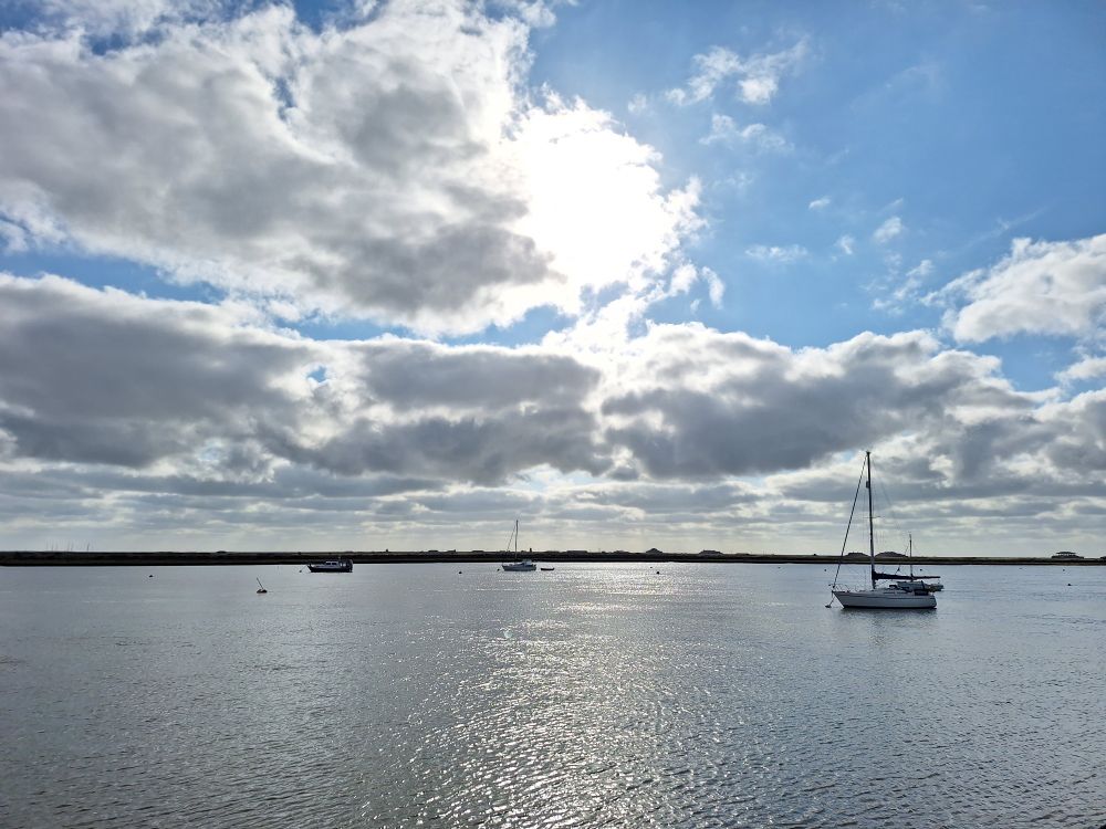 Image shows boats floating in the sea under a partially cloudy sky with the sun shining through the clouds 