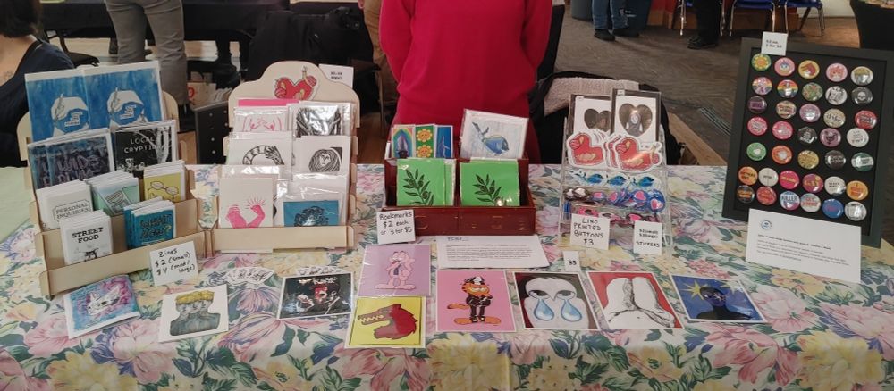 A table with an art market display of buttons, prints, zines and stickers.
