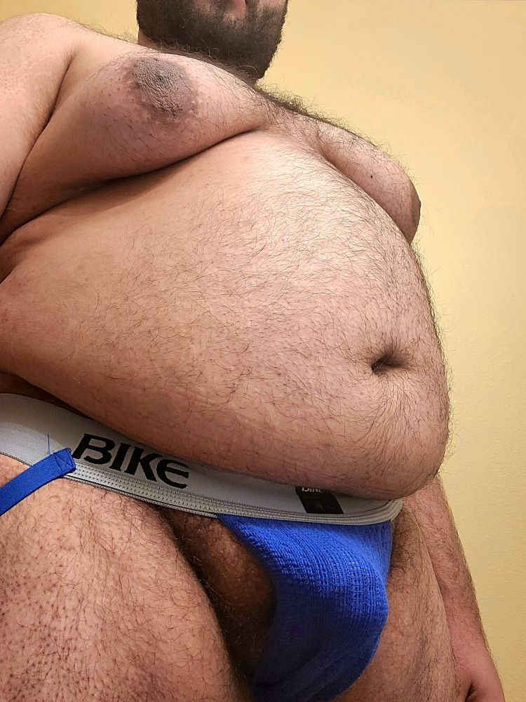 Chubby man is showing off his belly and moobs as his hard cock presses against the fabric of his jock.