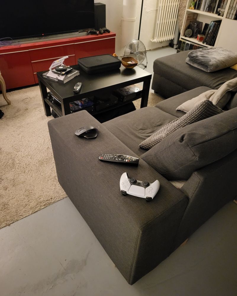 Accoudoir de 25cm de large de mon canap avec une telecommande, un manette PlayStation et une souris dessus