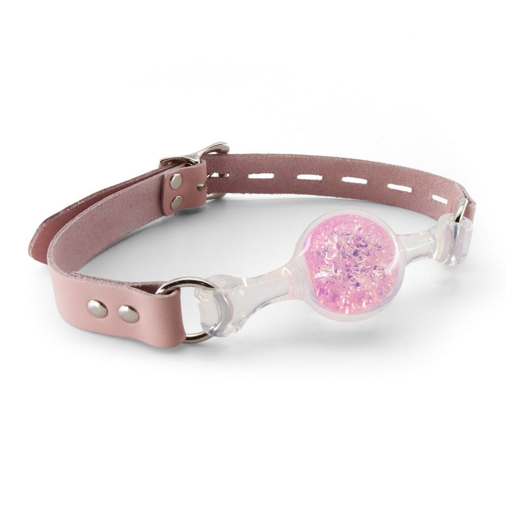 Ball gag made of transparent PVC, filled with pink sparkles in the ball section. The strap is made of dusty-pink leather. 