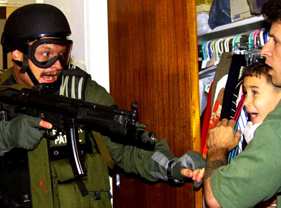 Image of a military goon hunting down tiny Elian Gonzales and finding him in his uncle's arms hiding in the closet 