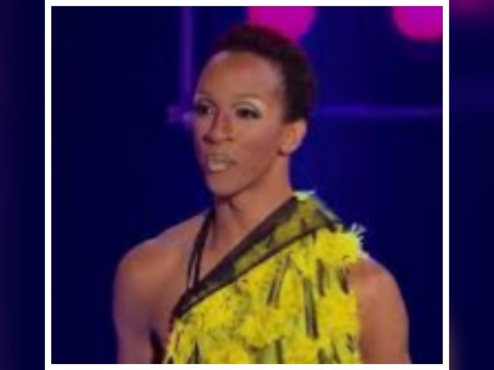 From Season 4 of RuPaul's Drag Race: Milan, a drag queen in a feathered yellow dress, a full face of makeup, and no wig. She looks disappointed. 