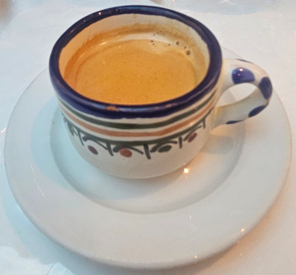 Une petite tasse d'espresso en céramique peinte est posée sur une soucoupe blanche. 