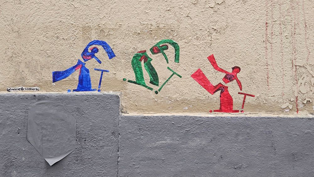 Ces trois silhouettes colorées (bleu, vert, rouge), réalisées en tape art, montrent des personnages en train d’effectuer des figures acrobatiques avec une trottinette. 

Le mouvement est stylisé et décomposé en trois poses différentes, un peu comme une séquence de tricks : rotation du corps, impulsion, réception… Le style est volontairement minimaliste, mais très dynamique.


