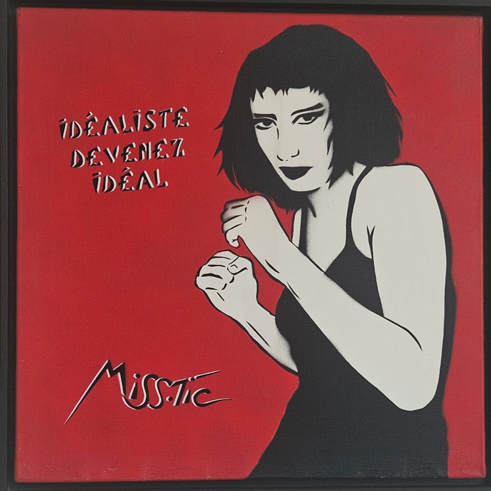 Description :

Sur un fond rouge intense, une femme en noir et blanc se tient en position de combat, les poings levés, symbole de force, de détermination et d’indépendance. Son regard perçant et son attitude assurée traduisent la résistance et l’émancipation féminine, thèmes chers à l’artiste.

À gauche de l’image, on peut lire l’inscription en lettres pochoirisées :
"Idéaliste, devenez idéal".
