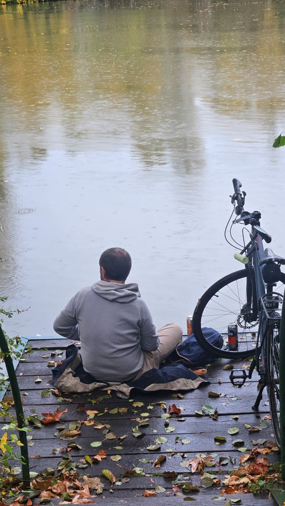 Un homme assis sur un ponton, à côté de son vélo. 