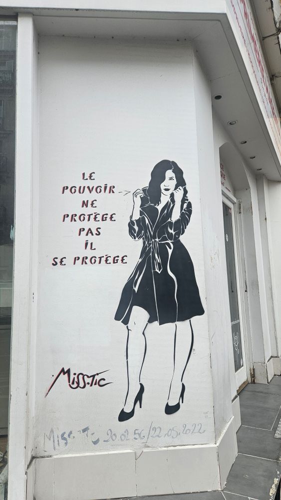 Ce Street Art est une fresque murale réalisée au pochoir par l’artiste française Miss.Tic, connue pour ses silhouettes féminines et ses aphorismes percutants.

On y voit une femme en imperméable ceinturée, aux cheveux bruns ondulés, portant des talons hauts. Elle adopte une posture assurée.

Cette femme est accompagnée de l'aphorisme :
« Le pouvoir ne protège pas, il se protège », un message fort et critique qui dénonce la nature du pouvoir politique ou social : au lieu d’assurer la protection des citoyens, il se protège lui-même.

La signature Miss.Tic apparaît en bas, accompagnée de dates peintes plus discrètement en dessous : 20.02.56 / 22.05.2022, qui correspondent à la date de naissance et de décès de l’artiste.
