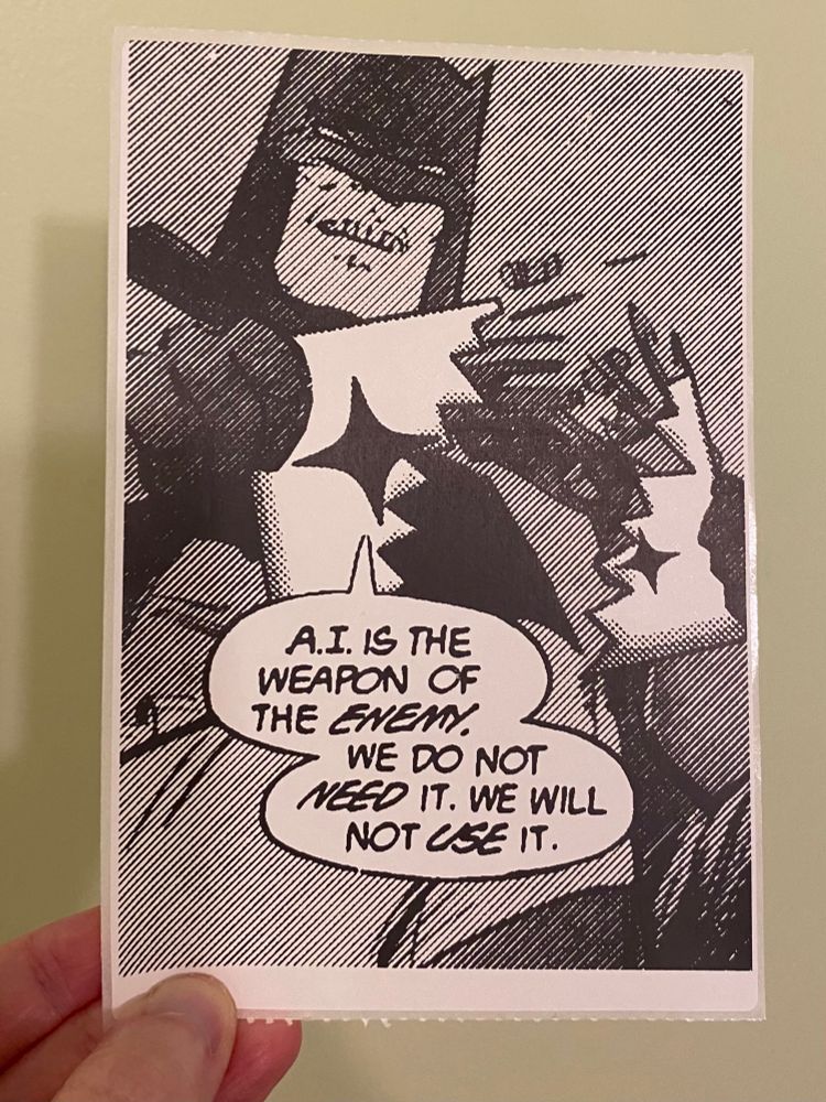 A thermal printed sticker the size of a mailing label. It's the Batman breaking a gun meme, converted into black and white and halftones. Batman is breaking a box with a sparkle icon on it and saying, "A.I. is the weapon of the enemy. We do not need it. We will not use it."