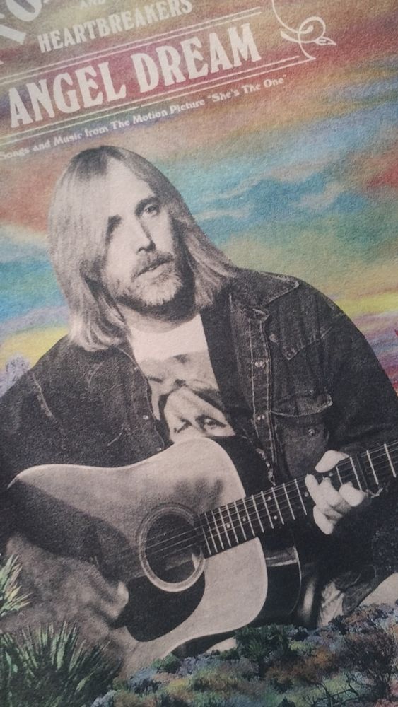 Album cover for Angel Dream with black and white Tom Petty playing guitar against a pastel rainbow of coloured clouds 