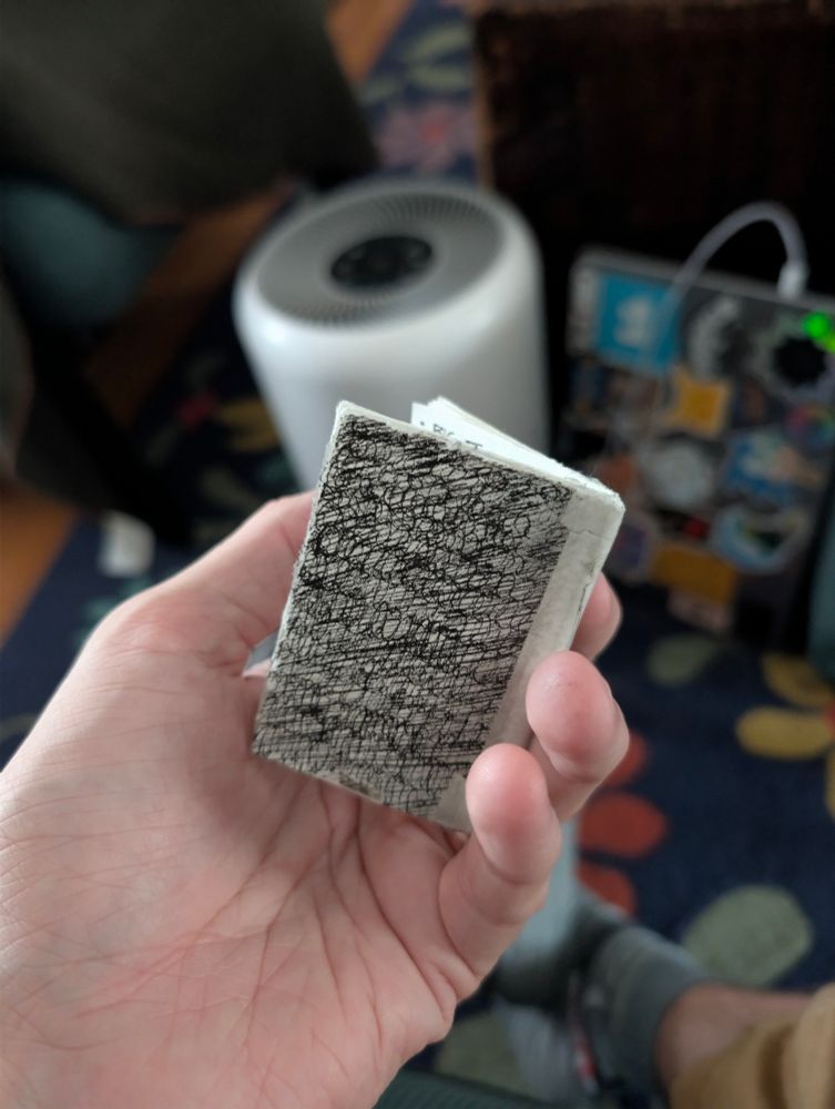 A hand holding a small, homemade book produced from folding a sheet of paper into 9 segments, and then stapling the center of the signature into a saddle stitch. This forms what is called in the industry a "soft spine," meaning, the entire book can be rolled up like a newspaper. 