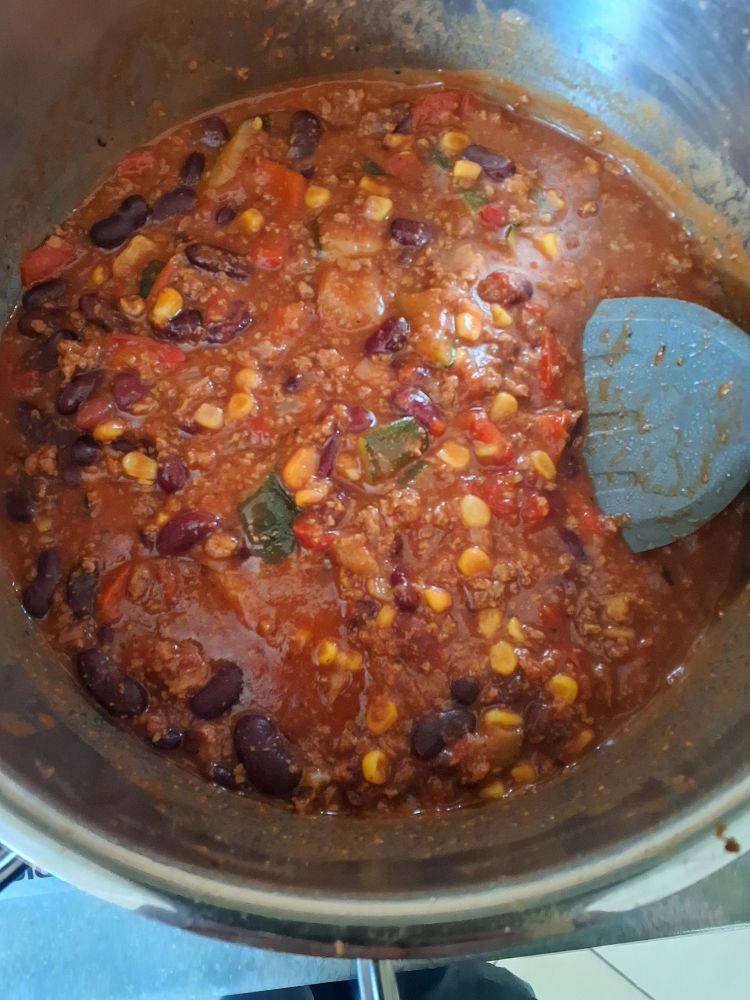 Blick in einen Topf mit Chili sin carne. Kidneybohnen, Mais, Paprika und Zucchini sind zu sehen. 