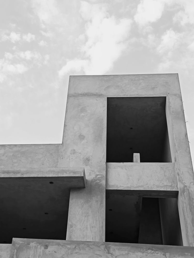 A black and white shot of an unfinished concrete building that has a beautiful asymmetry to it (in my opinion). Above are dispersed clouds