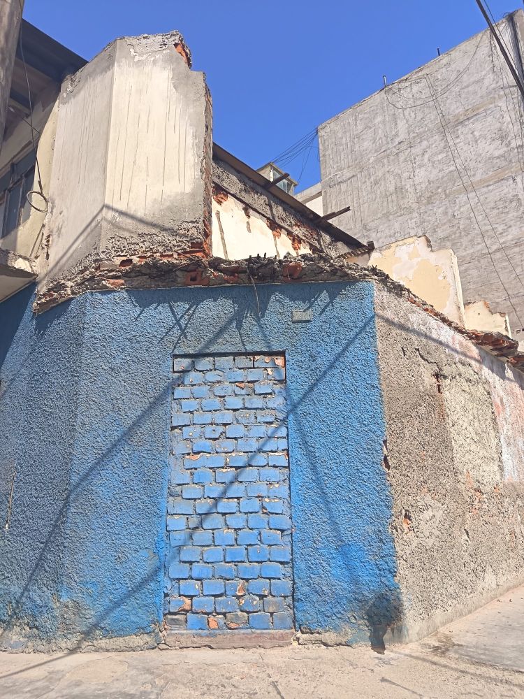 A building that with skewed angles and levels and materials. The front left wall is painted blue has a blue painted bricked up doorway