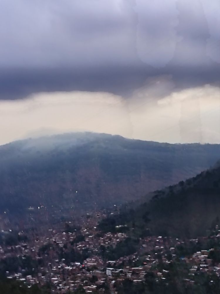 The view when arriving into Medellín, Colombia. Low lying lilacy clouds over mountains on all sides with the lights and buildings of Medellín in the valley. 