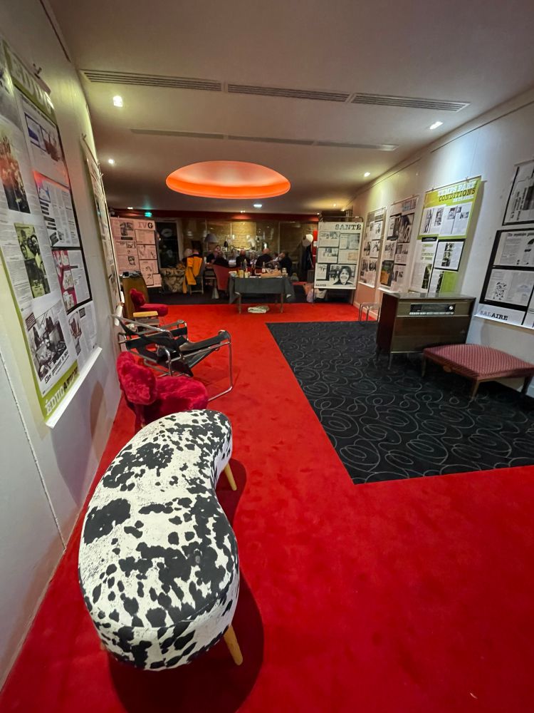 Salle de réunion au fond avec une très grande table et avant moquette rouge banquette en peau de vache et expo sur les murs