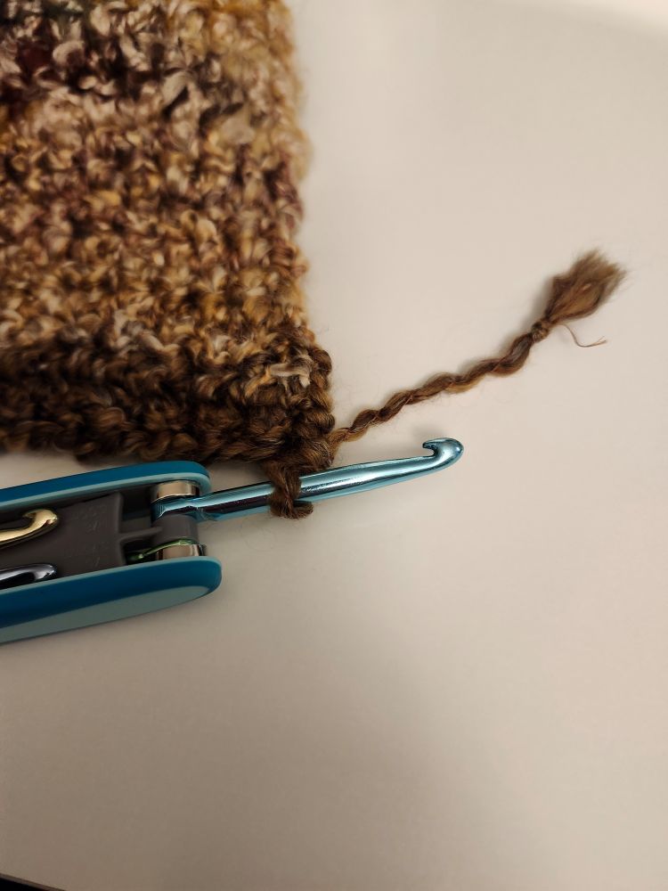 Blue crochet hook attached to a brown throw with about three inches of yarn left